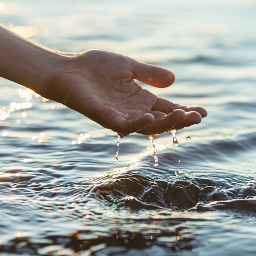 Eine Hand schöpt Wasser aus einem See